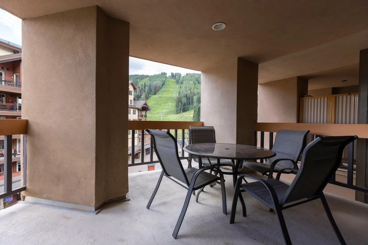 An inviting balcony with a table and chairs overlooking rolling mountains. The tranquil scene suggests a perfect spot for couples to relax, share meals, and soak in the sunset or sunrise together, with the soft light adding warmth and romance.