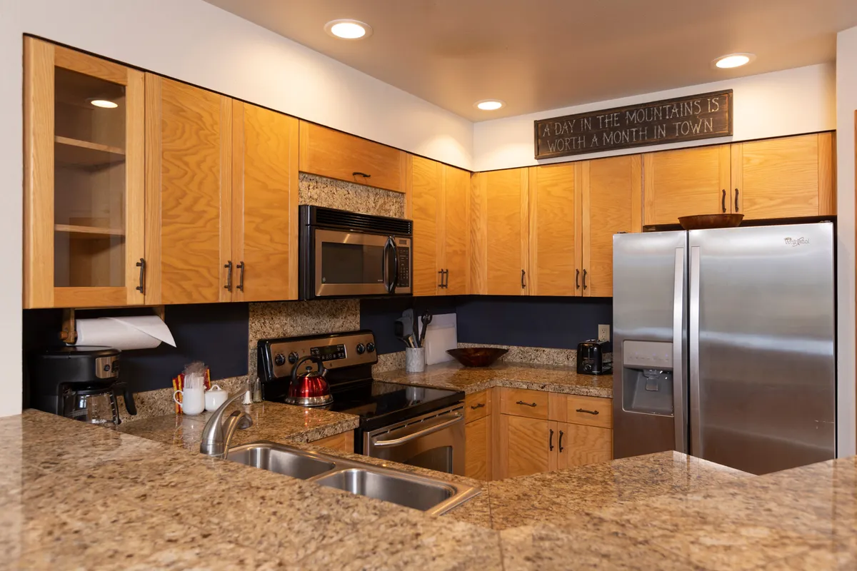 A warm, welcoming kitchen scene showcasing granite countertops, stainless steel appliances, wooden cabinetry, and a decorative sign. The space feels designed for group cooking, family meals, and festive baking sessions.