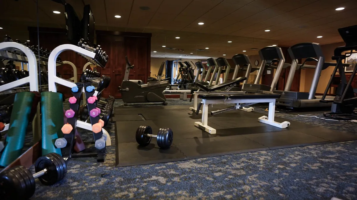 The fitness center is equipped with treadmills, dumbbells, and stretching mats, offering a bright, motivating space for workouts and group fitness activities.