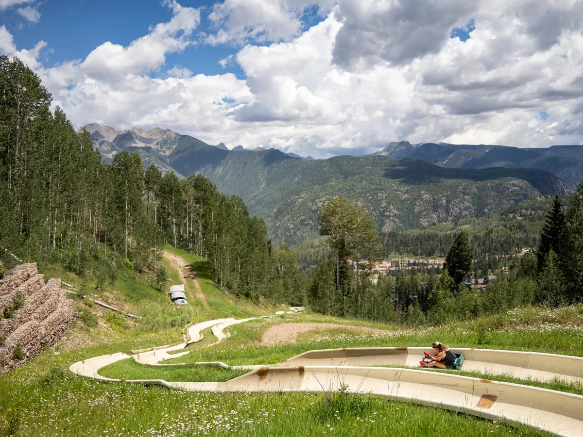 This exterior image captures a panoramic view of a mountain range with a slide pathway, a person seated nearby, and open green spaces. The scene evokes a sense of outdoor adventure and the alpine environment surrounding Kendall 437.